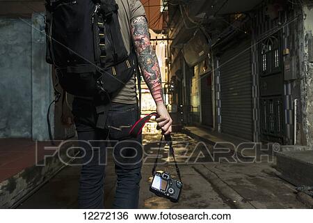 A male traveler carrying his camera down a narrow street; Xiamen, Fujian, China View Large Photo Image Stock Photograph - A male traveler carrying his camera down a narrow street; Xiamen, Fujian, China. Fotosearch