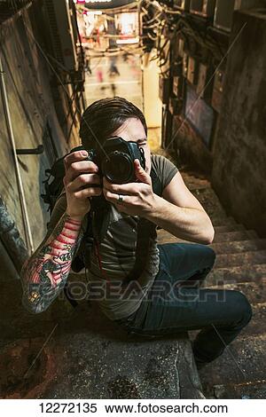 Stock Photography - A male traveler taking a photograph with his camera in a narrow street; Xiamen, Fujian, China. Fotosearch
