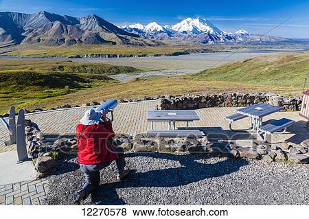 Stock Photo - A male visitor views Mt. McKinley through the park provided scope at Eielson Visitor Center in Denali National Park, Interior Alaska, Summer, USA.. Fotosearch