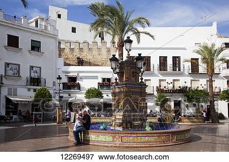 Stock Photo - A man and baby sit a water fountain in a town square; Vejer de la Frontera, Andalusia, Spain. Fotosearch