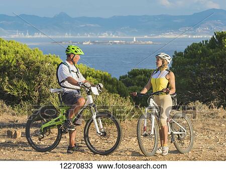 A man and woman on bicycles stand with a view of the ocean and coastline; Tarifa, Cadiz, Andalusia, Spain View Large Photo Image Stock Image - A man and woman on bicycles stand with a view of the ocean and coastline; Tarifa, Cadiz, Andalusia, Spain. Fotosearch