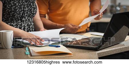 Stock Photograph - A man and woman standing in the kitchen working together with documents and a computer; Regina, Saskatchewan, Canada. Fotosearch