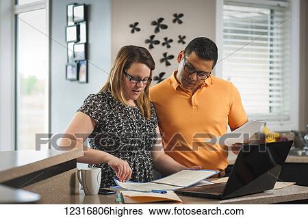 Stock Photograph - A man and woman standing in the kitchen working together with documents and a computer; Regina, Saskatchewan, Canada. Fotosearch