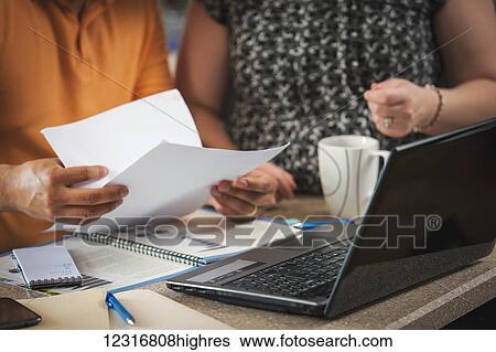 Stock Photograph - A man and woman standing in the kitchen working together with documents and a computer; Regina, Saskatchewan, Canada. Fotosearch