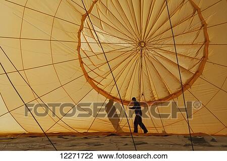 Stock Image - A man checks ropes inside a hot air balloon as it lies on the ground being inflated; Filzmoos, Austria. Fotosearch