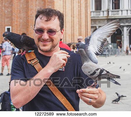 Stock Photo - A man feeds the pigeons in Piazza San Marco; Venice, Italy. Fotosearch