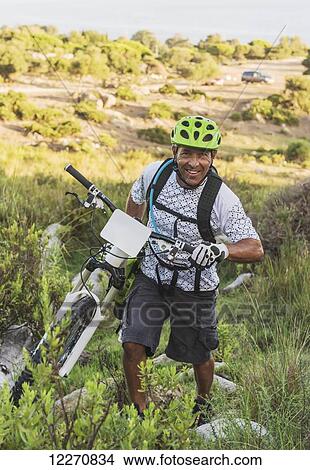 Picture - A man pulls his bike over rugged terrain; Tarifa, Cadiz, Andalusia, Spain. Fotosearch