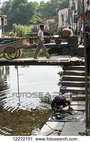 A man pulls his wooden cart and a woman works by the water's edge in a small village near Wuyuan; Jiangxi province, China View Large Photo Image Stock Image - A man pulls his wooden cart and a woman works by the water's edge in a small village near Wuyuan; Jiangxi province, China. Fotosearch