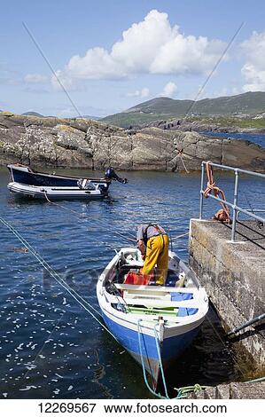 Stock Photo - A man stands in his boat by the pier preparing for fishing, near Caherdaniel; County Kerry, Ireland. Fotosearch
