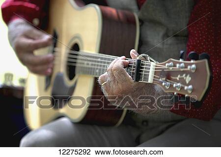 Stock Image - A man's hands playing a guitar with his fretting hand in focus and his strumming hand out of focus; United States of America. Fotosearch