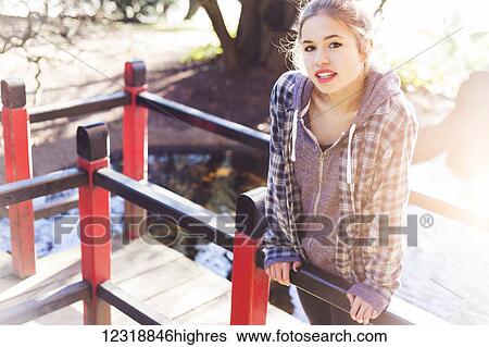 Stock Photograph - A pretty teenage girl makes a playful pose on a boardwalk in the park with sunlight from behind; New Westminster, British Columbia, Canada. Fotosearch