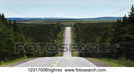 Stock Photograph - A road dips down into a valley and comes back up again and leads into the distance; Pleasant Bay, Nova Scotia, Canada. Fotosearch