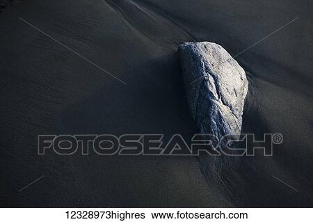A rock sits on the dark, wet sand; Alaska, United States of America View Large Photo Image Stock Photograph - A rock sits on the dark, wet sand; Alaska, United States of America. Fotosearch