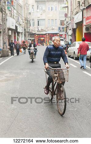 Picture - A senior man cycling in a downtown street; Xiamen, Fujian province, China. Fotosearch