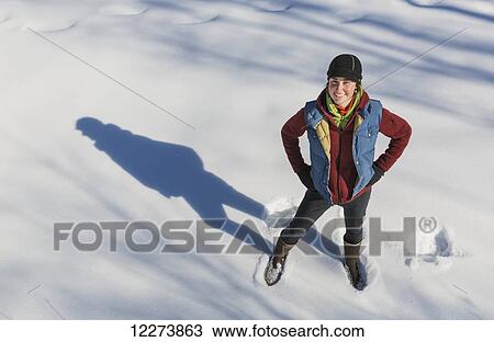 Stock Image - A smiling young woman wearing a hat and gloves stands in a snowbank, Winter, Southcentral Alaska, USA. Fotosearch