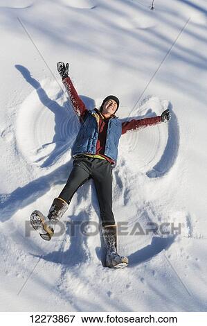 Stock Photo - A smiling young woman wearing a hat and gloves makes a snow angel in a snowbank, Winter, Southcentral Alaska, USA. Fotosearch