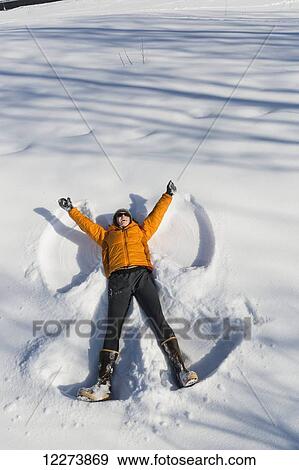 Stock Photo - A smiling young woman wearing a hat and gloves makes a snow angel in a snowbank, Winter, Southcentral Alaska, USA. Fotosearch