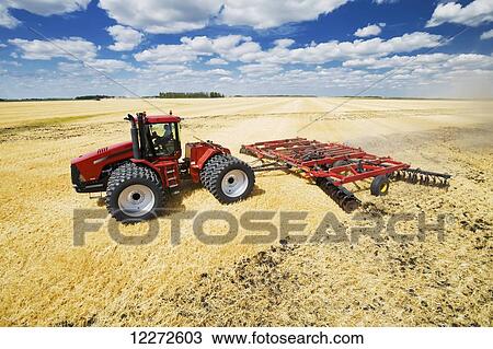 Stock Image - A tractor pulling a disc harrow works soil containing barley stubble, near Lorette; Manitoba, Canada. Fotosearch
