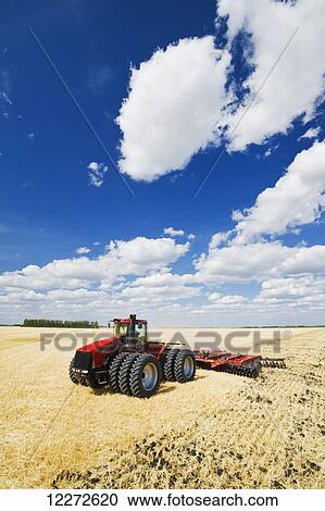 Stock Image - A tractor pulling a disc harrow works soil containing barley stubble, near Lorette; Manitoba, Canada. Fotosearch
