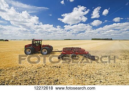 Stock Photo - A tractor pulling a disc harrow works soil containing barley stubble, near Lorette; Manitoba, Canada. Fotosearch