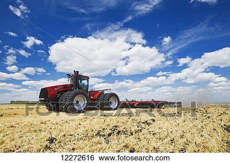 Stock Photograph - A tractor pulling a disc harrow works soil containing barley stubble, near Lorette; Manitoba, Canada. Fotosearch
