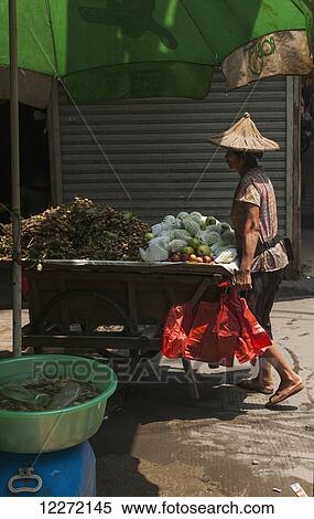 Stock Photography - A woman carries her cart full of fruits, Xiamen Local Market; Xiamen, Fujian Province, China. Fotosearch