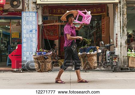 Stock Photo - A woman carrying her shopping purchases with the typical bamboo stick, very common in China; Xiamen, Fujian Province, China. Fotosearch