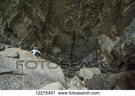 Stock Image - A woman sits at the entrance to a large cave in Toro Toro National Park; Bolivia. Fotosearch