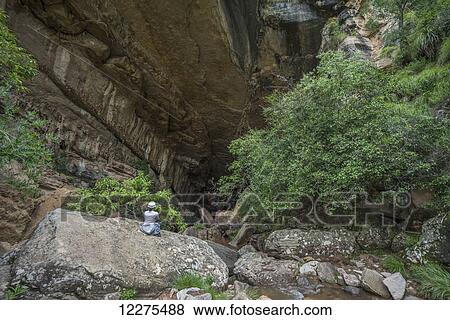 Stock Photo - A woman sits at the entrance to a large cave in Toro Toro National Park; Bolivia. Fotosearch