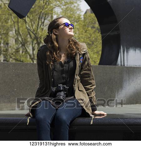 A woman sits on a bench in an urban park looking up with trees and a sculpture in the background; New York City, New York, United States of America View Large Photo Image Stock Photograph - A woman sits on a bench in an urban park looking up with trees and a sculpture in the background; New York City, New York, United States of America. Fotosearch