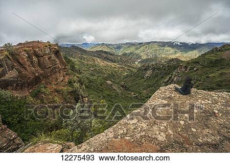 Stock Image - A woman sits on a rock looking out over the beautiful landscape of Toro Toro National Park; Bolivia. Fotosearch