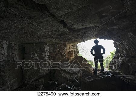 Stock Image - A woman stands silhouetted against the bright sky outside of a very large cave deep within Toro Toro National Park; Bolivia. Fotosearch