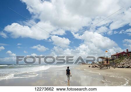 Stock Image - A woman walks on the wet sand of the beach in bare feet holding her shoes; Aguas Dulces, Uruguay. Fotosearch