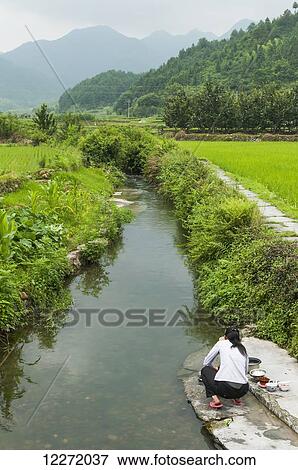 A woman washing dishes along a stream in a village near Wuyuan; Jiangxi province, China View Large Photo Image Stock Photo - A woman washing dishes along a stream in a village near Wuyuan; Jiangxi province, China. Fotosearch