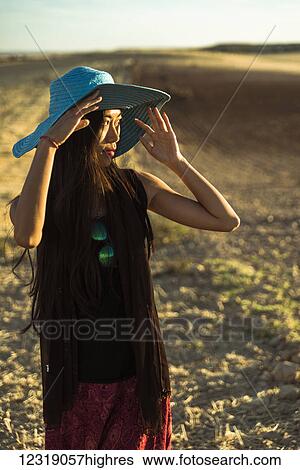 Stock Photograph - A young Asian woman walking in a golden wheat field; Madrid, Spain. Fotosearch