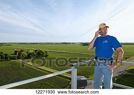 A young farmer talks on his cell phone atop a grain bin with a farmstead and fields in the background, near Northrop; Minnesota, United States of America View Large Photo Image Stock Image - A young farmer talks on his cell phone atop a grain bin with a farmstead and fields in the background, near Northrop; Minnesota, United States of America. Fotosearch