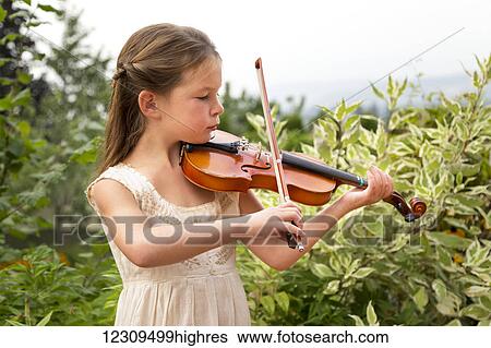 Stock Photograph - A young girl playing a violin in her yard; Salmon Arm, British Columbia, Canada. Fotosearch