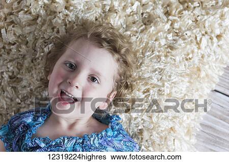 A young girl with curly blond hair lays on the floor on a soft rug playfully looking into the camera and laughing; St. Albert, Alberta, Canada View Large Photo Image Stock Photograph - A young girl with curly blond hair lays on the floor on a soft rug playfully looking into the camera and laughing; St. Albert, Alberta, Canada. Fotosearch