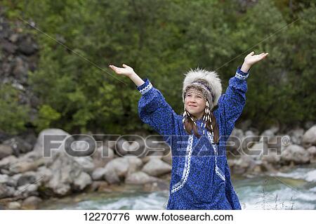 Stock Photograph - A young Inupiat tween girl in a traditional Eskimo Kuspuk and native headdress with outstretched arms, Hatcher Pass, Palmer, Southcentral, Summer. Fotosearch