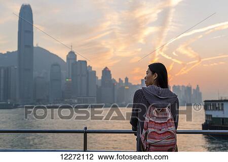 A young woman at the waterfront with a view of the skyline at sunset, Kowloon; Hong Kong, China View Large Photo Image Stock Image - A young woman at the waterfront with a view of the skyline at sunset, Kowloon; Hong Kong, China. Fotosearch
