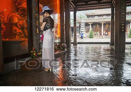 Stock Photograph - A young woman praying in Nan Pu Tuo Temple to the Buddhist Guardians; Xiamen, Fujian Province, China. Fotosearch
