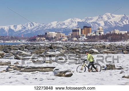 Stock Photo - A young woman pushes her studded tire bicycle amongst the ice chunks in the Cook Inlet next to the Tony Knowles Coastal Trail, Anchorage, Southcentral Alaska, USA.. Fotosearch