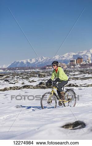 Picture - A young woman rides a studded tire bicycle next to the Tony Knowles Coastal Trail, Anchorage, Southcentral Alaska, USA.. Fotosearch