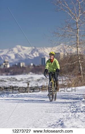 Stock Photo - A Young Woman rides a studded tire bicycle down the Tony Knowles Coastal Trail, Anchorage, Southcentral Alaska, USA.. Fotosearch