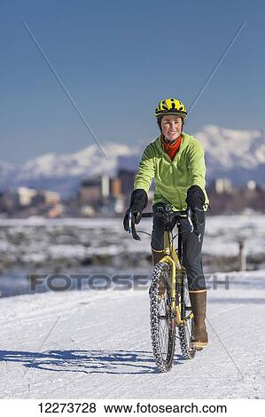 Stock Photo - A Young Woman rides a studded tire bicycle down the Tony Knowles Coastal Trail, Anchorage, Southcentral Alaska, USA.. Fotosearch