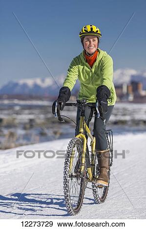 Stock Photo - A Young Woman rides a studded tire bicycle down the Tony Knowles Coastal Trail, Anchorage, Southcentral Alaska, USA.. Fotosearch
