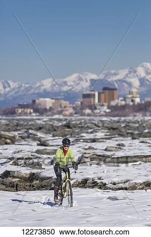 Stock Image - A young woman rides her studded tire bicycle amongst the ice chunks in the Cook Inlet next to the Tony Knowles Coastal Trail, Anchorage, Southcentral Alaska, USA.. Fotosearch