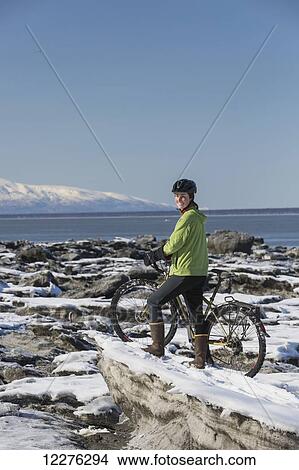 A young woman stands with her bicycle on ice next to the Tony Knowles Coastal Trail, Anchorage, Southcentral Alaska, USA. View Large Photo Image Picture - A young woman stands with her bicycle on ice next to the Tony Knowles Coastal Trail, Anchorage, Southcentral Alaska, USA.. Fotosearch