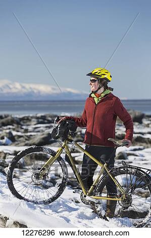 Stock Photograph - A young woman stands with her bicycle on ice next to the Tony Knowles Coastal Trail, Anchorage, Southcentral Alaska, USA.. Fotosearch
