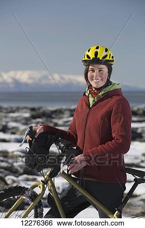 Stock Photograph - A young woman stands with her bicycle on ice next to the Tony Knowles Coastal Trail, Anchorage, Southcentral Alaska, USA.. Fotosearch